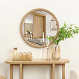 A decorative mirror with a circular design hangs above a wooden console table. On the table sit a vase with leafy branches, two tall candlesticks, and a tray with a pitcher and glasses, creating an inviting tableau.