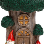 A close-up of a whimsical gnome tree house with a round window, arched door, and two decorative gnomes wearing red hats at the base¡ªperfect inspiration for outdoor space decor.