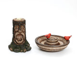 A tree trunk-shaped candle holder, resembling a brown old man, features a carved face and a decorative dish with two small red bird figurines. This charming piece serves as an outdoor decor centerpiece and adds whimsical beauty to any space.