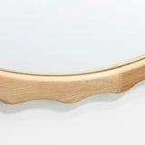 A close-up of a round mirror with an elegant scalloped design, framed in rich rubberwood.