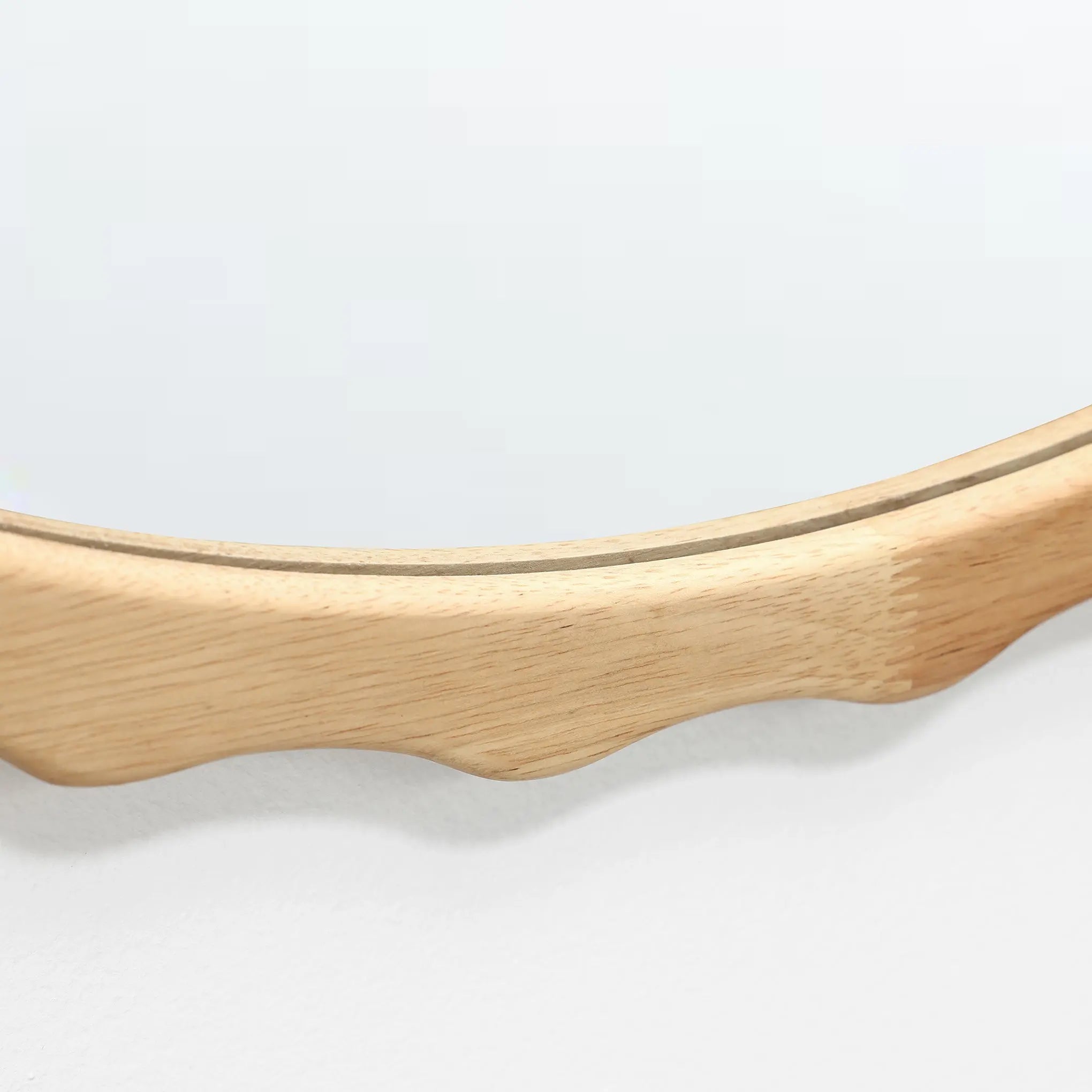 A close-up of a round mirror with an elegant scalloped design, framed in rich rubberwood.