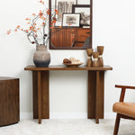 Wooden console table with decorative vases, a bowl of orbs, and a mirror reflecting artwork. Its minimalist design complements the mid-century modern aesthetic. A chair is partially visible on the right.
