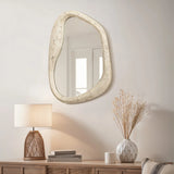 As an eye-catching piece of home decor, this asymmetrical mirror with a free-form frame hangs above a wooden console. Positioned elegantly beside a lamp and a vase with dried flowers, its unique design adds charm and sophistication to any space.