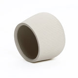 The LuxenHome Ribbed Round Planter, standing at 10.63 tall, lies tilted against a white background. This large off-white planter showcases modern minimalist design with its textured ribbed exterior and smooth circular opening.