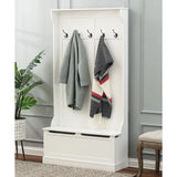 A white hall tree with a built-in storage bench features four black hooks acting as a coat rack, holding two jackets and a scarf. Nearby, a green plant and an upholstered chair complete the inviting entryway scene.