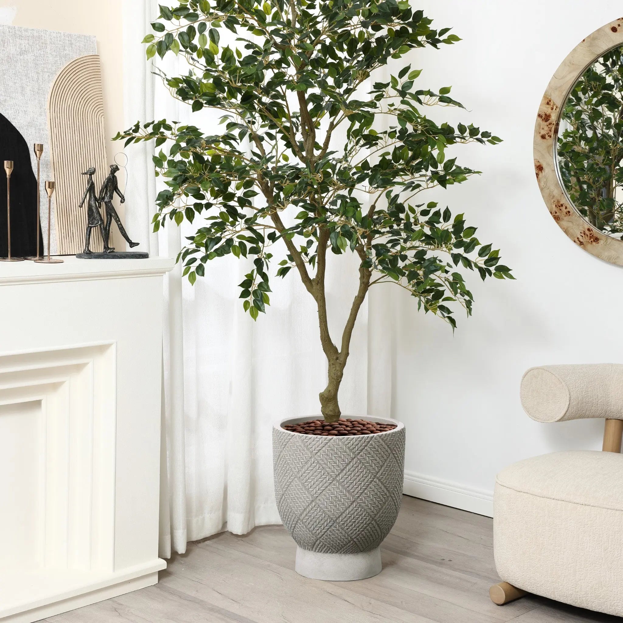 A potted tree in a grey MgO material planter stands in a minimalist living room next to a chair and white fireplace. A round mirror and modern decor, along with a cleverly designed drainage hole, complete the serene backdrop.