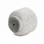 A textured, light gray cylindrical vase lying on its side with a small hole in the base adds a touch of retro minimalist decor.