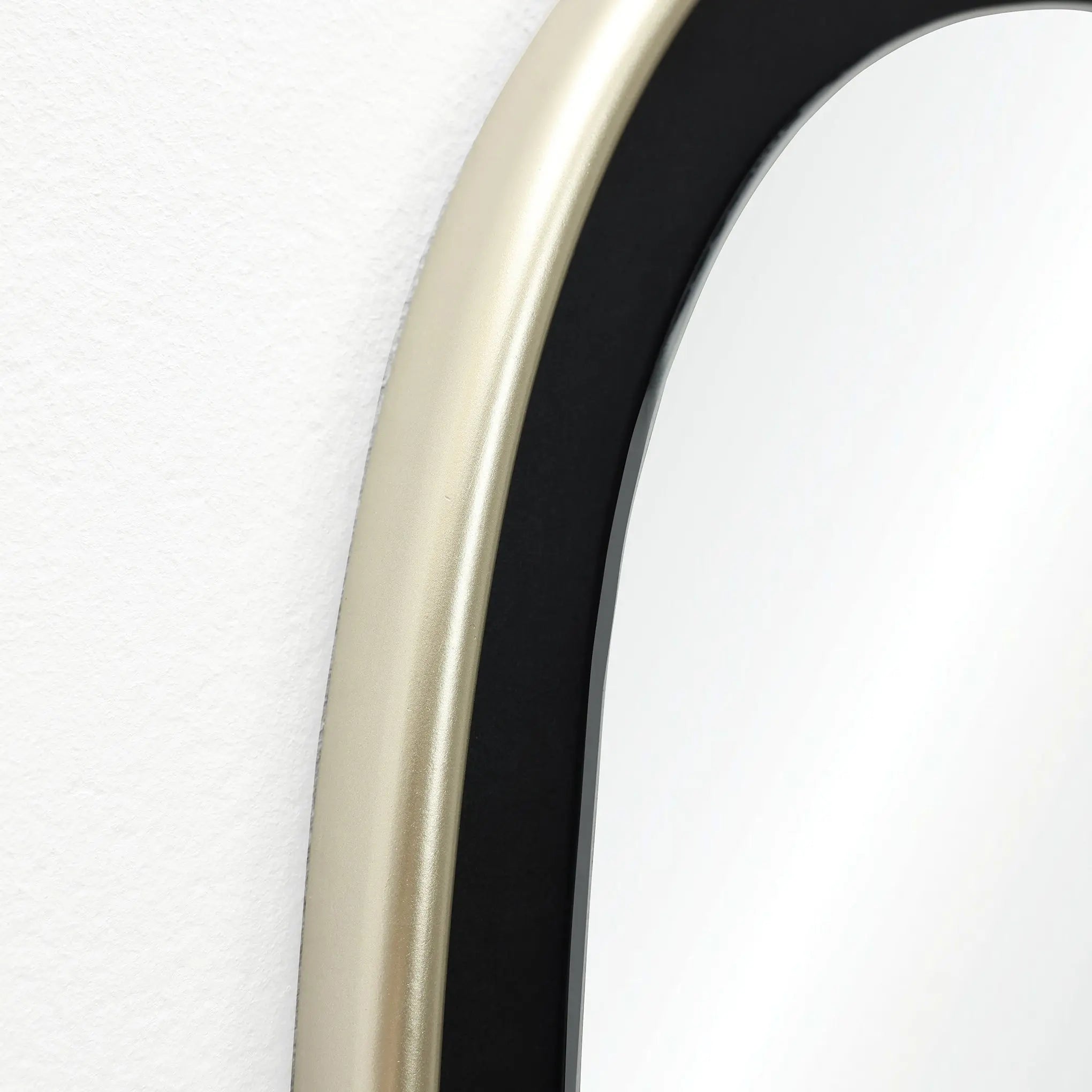 Close-up of an oblong-shaped, contemporary mirrors edge with a striking gold and black frame against a pristine white wall.