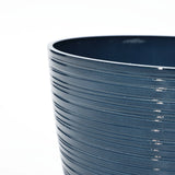 Close-up of a dark blue, glossy ceramic pot featuring a horizontal ribbed texture against a white background. This decorative planter is perfect for indoor and outdoor use, boasting a UV-protected finish that ensures lasting beauty in any setting.