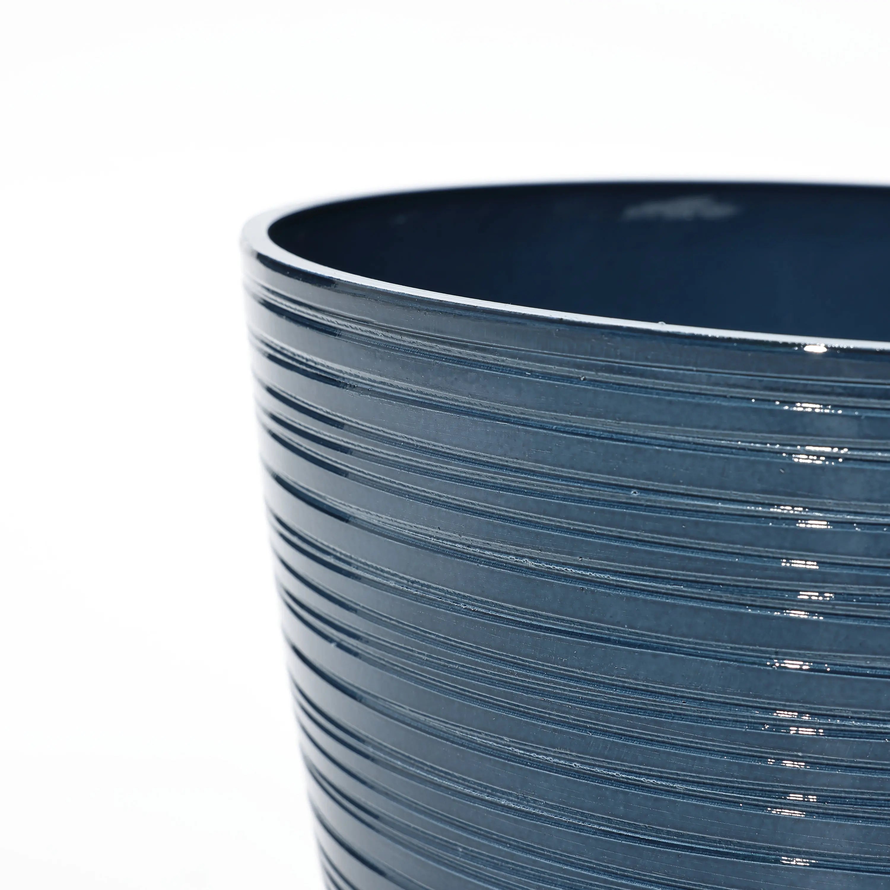Close-up of a dark blue, glossy ceramic pot featuring a horizontal ribbed texture against a white background. This decorative planter is perfect for indoor and outdoor use, boasting a UV-protected finish that ensures lasting beauty in any setting.
