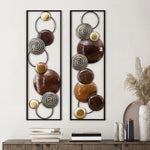 Two vertical handcrafted panels featuring circular metallic and glossy brown elements serve as striking metal wall decor above a console table adorned with vases, books, and dried plants—perfect for contemporary home décor.
