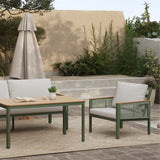 Outdoor patio set with a durable aluminum alloy frame, wooden table, plush-cushioned loveseat sofa, and chair on a rug. Stone steps and greenery are in the background.