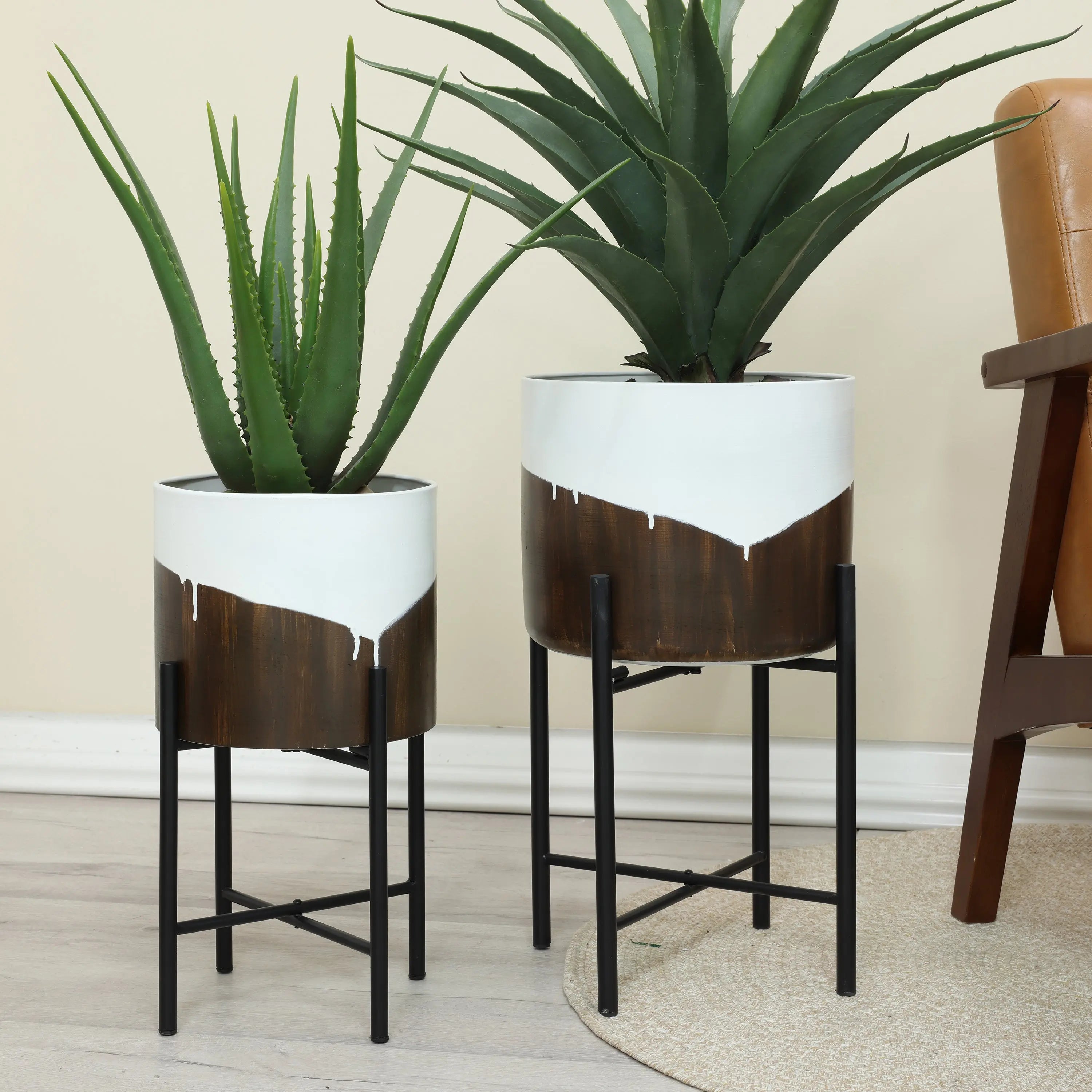 Two indoor plants in stylish white and brown pots on sleek metal stands create a unique dynamic visual effect, enhancing the home decor. They rest gracefully on a wooden floor next to a chair, blending elegance with contemporary flair.