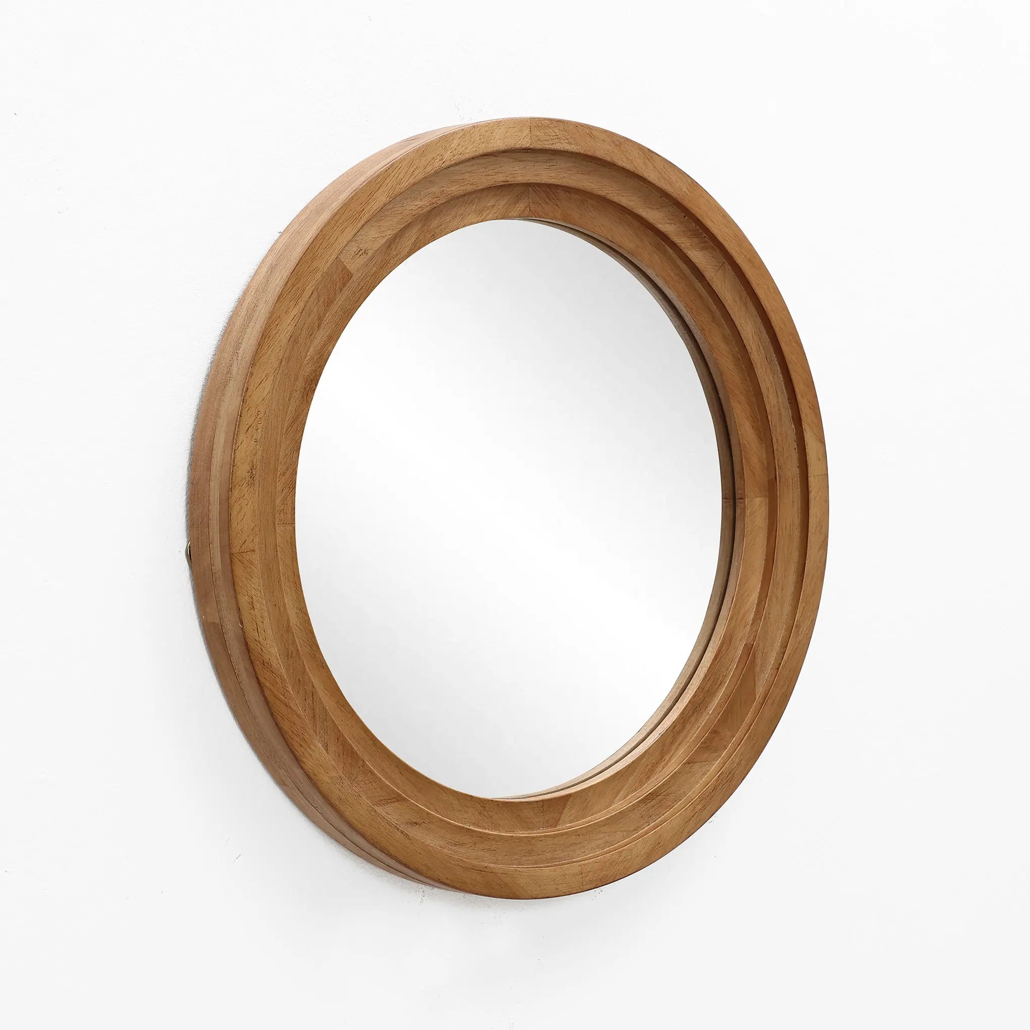 A round rubberwood framed mirror with a thick wooden border is elegantly mounted on a white wall, creating an optical illusion of expanded space.