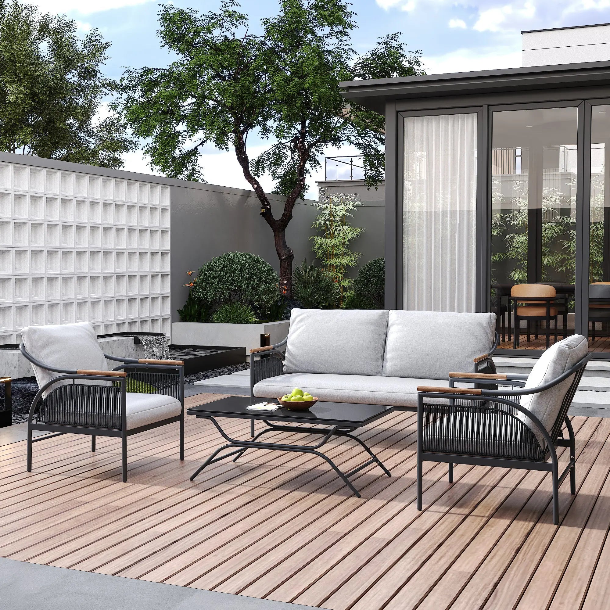 Modern outdoor patio featuring an outdoor seating set with a sofa, two chairs adorned with removable waterproof cushions, and a table on a wooden deck. A tree and plants create a lush backdrop, while a sliding glass door offers easy access inside.