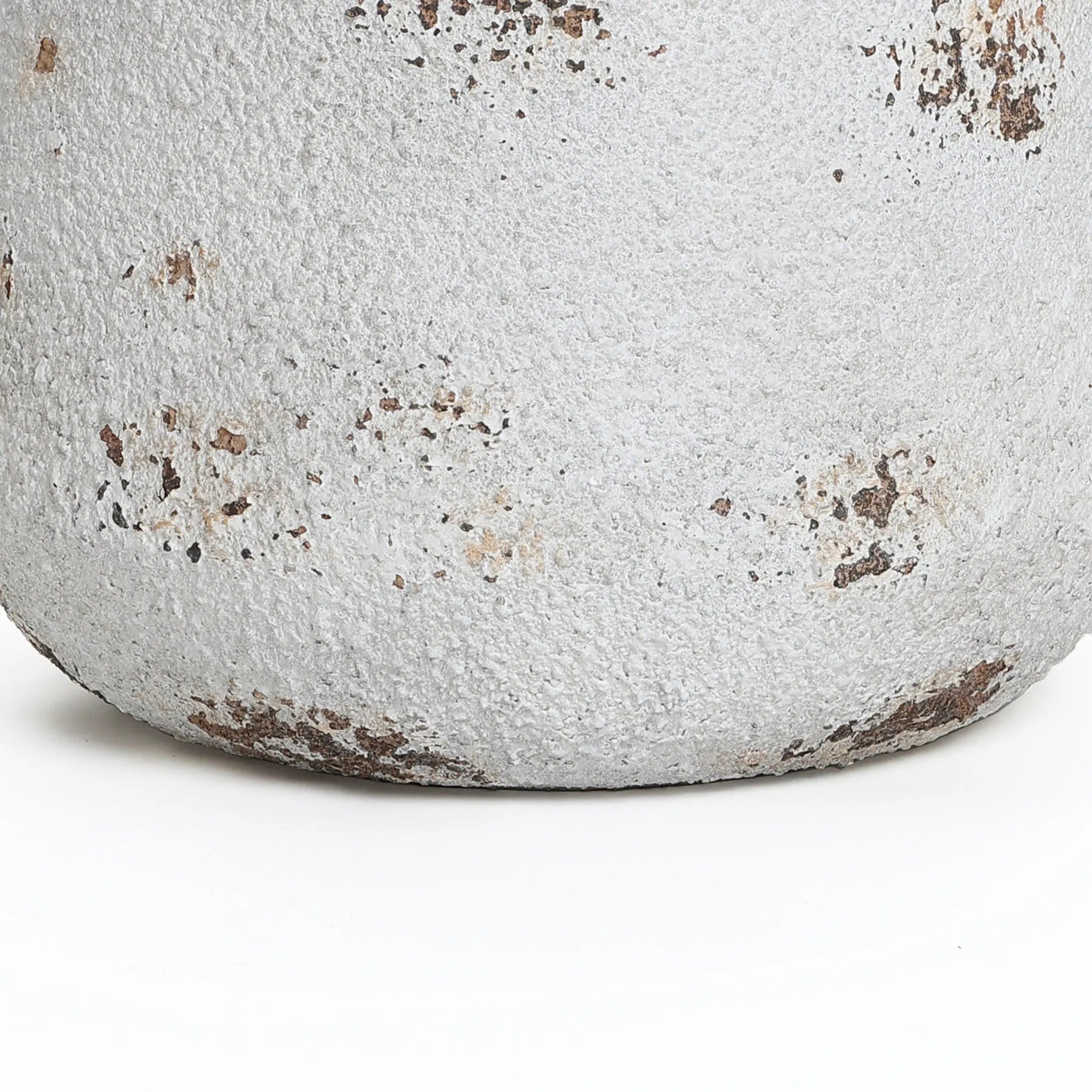 A close-up of the base of a round planter reveals its weathered, textured white surface, highlighted by patches of peeling paint and spots of rust. Its vintage minimalist style is beautifully accentuated, set against a plain white background.