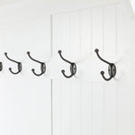 A row of four black metal coat hooks, part of a stylish coat rack, mounted on a white paneled wall.