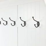 A row of four black metal coat hooks, part of a stylish coat rack, mounted on a white paneled wall.