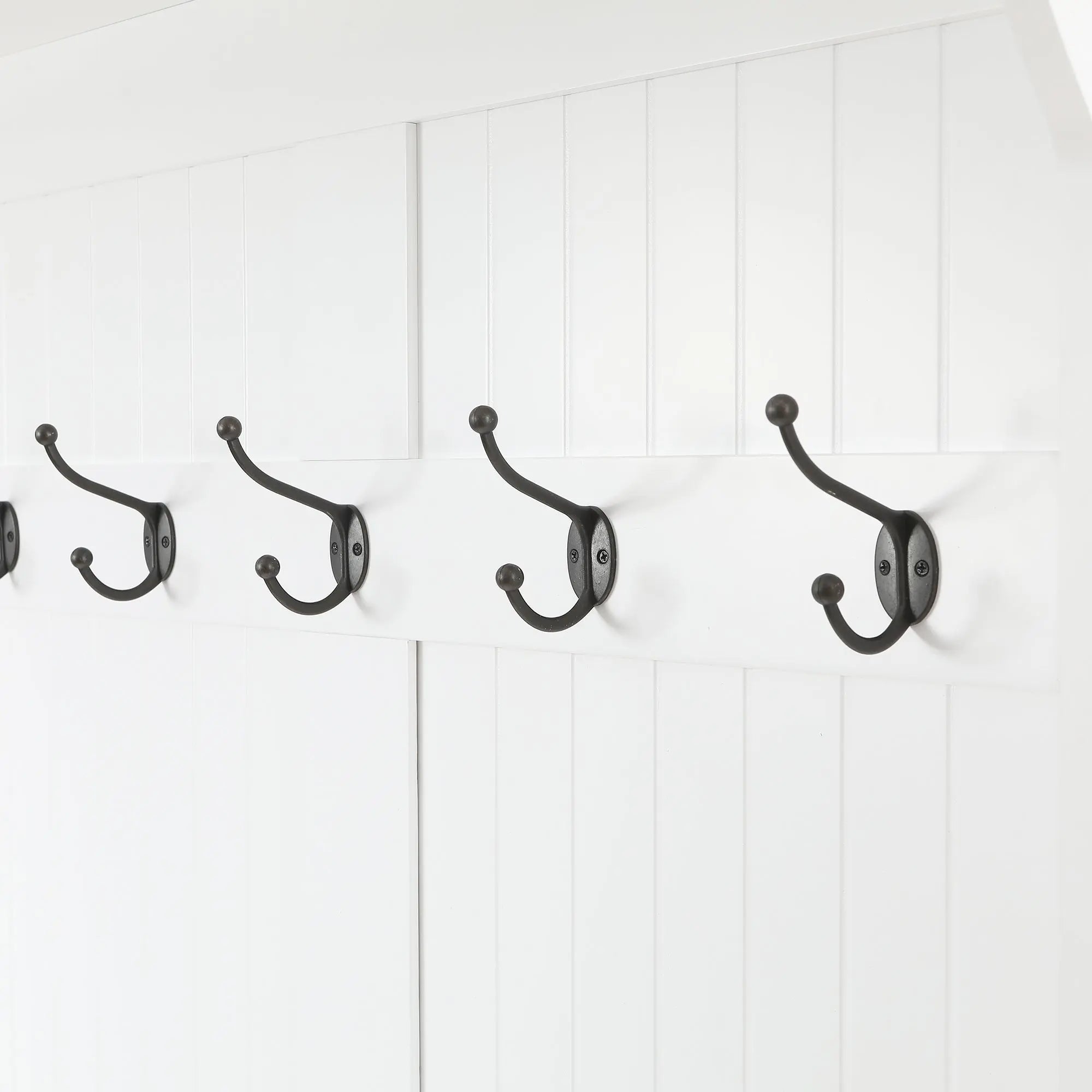 A row of four black metal coat hooks, part of a stylish coat rack, mounted on a white paneled wall.