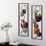 Two rectangular handcrafted panels feature circular and spiral designs in brown, gold, and silver tones. This metal wall decor hangs above a black console table with a pink vase and stacked books, perfect for contemporary home décor.