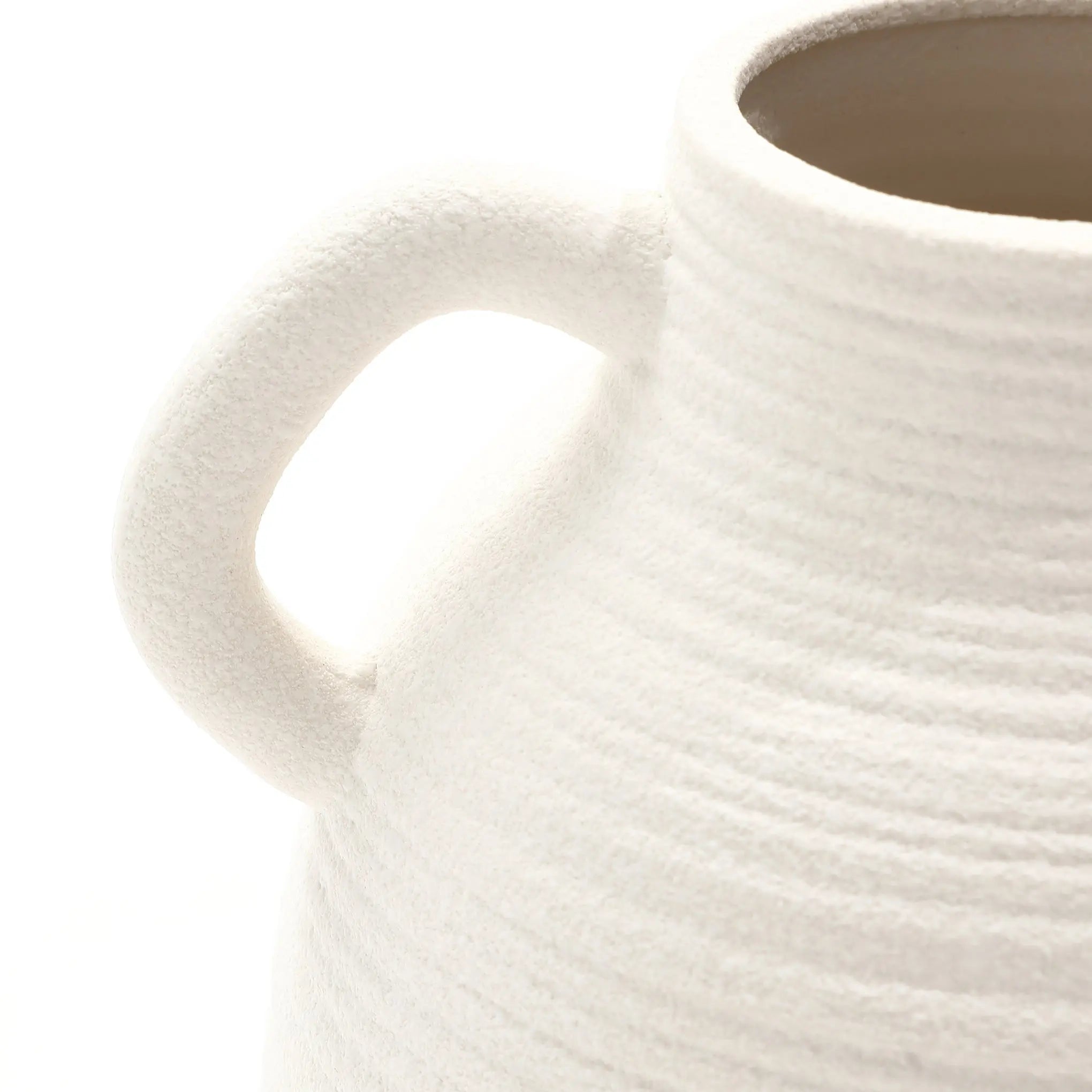 Close-up of a textured, white ceramic vase with a single handle and vintage charm. The vase boasts a ribbed pattern and smooth interior, captured against a plain white background.