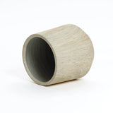 A cylindrical, light-colored wooden cup is placed on its side against a plain white background, resembling a minimalist touch to any indoor outdoor planter setup.