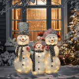 Three illuminated snowmen with black-and-white scarves stand outside a house at night, serving as charming outdoor Christmas decor in front of a window with festive lights and snow-covered decorations.