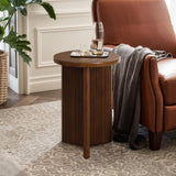 A round tabletop crafted from high-quality MDF wood with a fluted base holds a tray with a water bottle and glass, positioned beside a brown leather armchair. A gray blanket is draped over the chair, enhancing the cozy vibe of this mid-century modern side table setup.