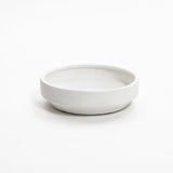 A plain, round ceramic vase seamlessly melds with a white background.