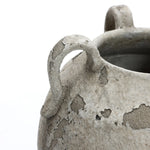 A close-up of the aged, textured LuxenHome rustic gray and white terracotta vase with handles, 11 h, highlights its curved handle and upper rim. It showcases weathered details against a plain background, blending handcrafted charm with contemporary elegance.