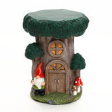 A decorative gnome tree house figurine featuring a tree stump house with a round window, door, two mushrooms, and a gnome beside it¡ªperfect for adding charm to your outdoor space decor. Set against a white background.