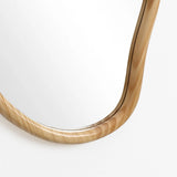Close-up of a corner of an irregularly shaped mirror with a smooth, natural pine wood frame. This decorative statement piece stands out against the white background.