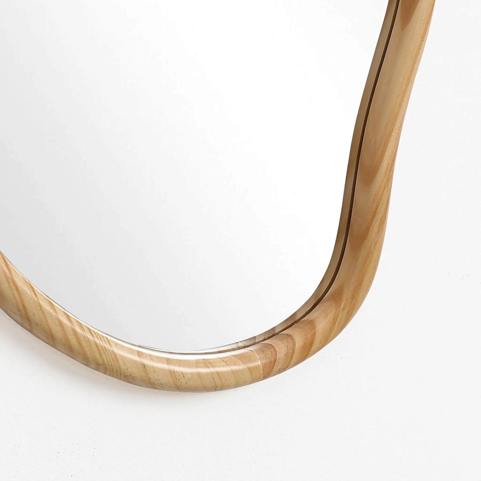 Close-up of a corner of an irregularly shaped mirror with a smooth, natural pine wood frame. This decorative statement piece stands out against the white background.