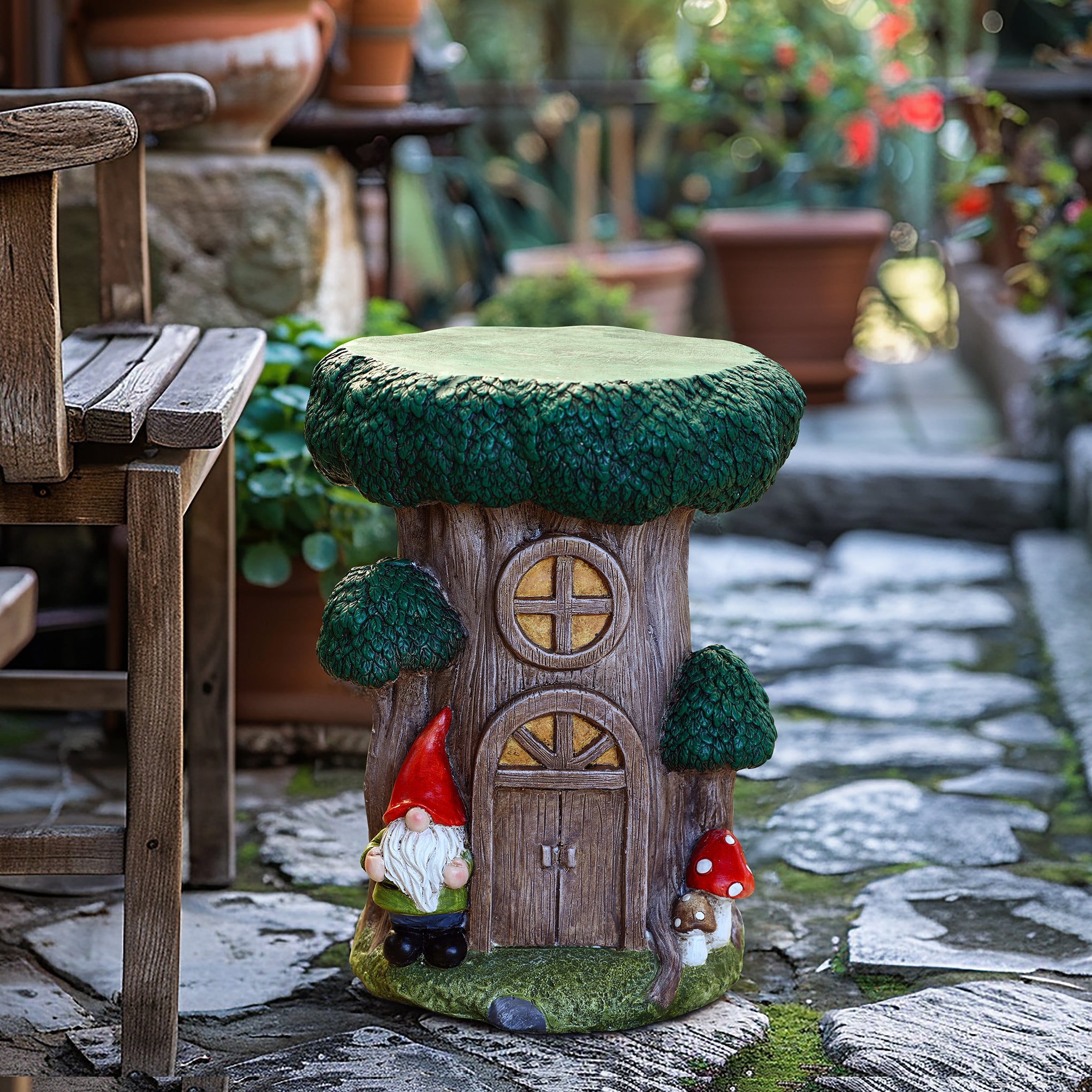 A whimsical gnome tree house garden stool with windows, a door, and two gnome figurines stands on a stone patio beside potted plants and a wooden bench, adding playful charm to your outdoor space decor.