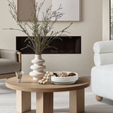 A modern living room showcases a wooden table with a round bowl vase and branches. A comfortable white armchair and a minimalist decor featuring an indoor and outdoor vase complete this serene setting.