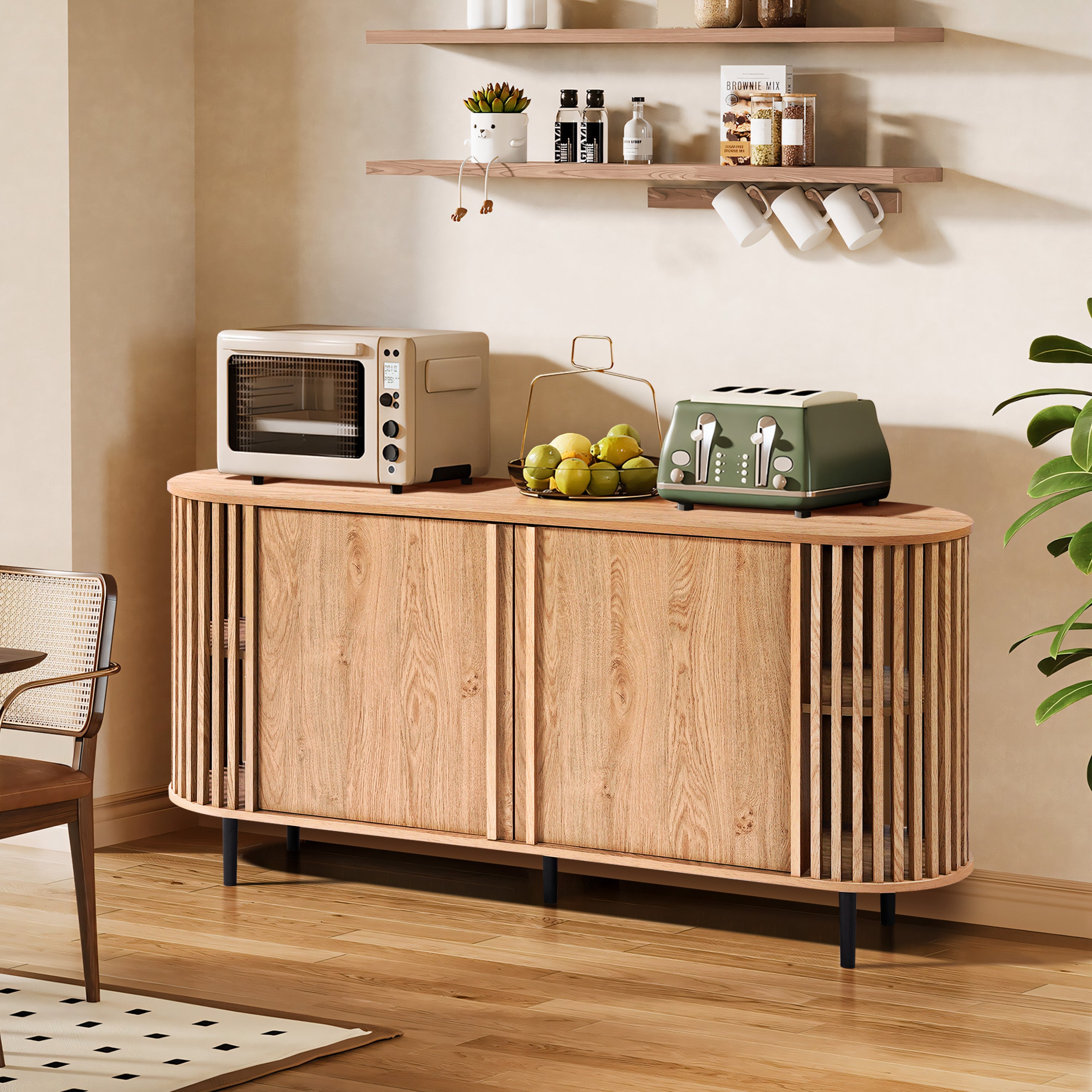 In a modern kitchen setting, an oak wood grain finish mid-century modern buffet cabinet complements the toaster, oven, and bowl of lemons. Two shelves above hold mugs and spices, while a plant stands gracefully to the right.