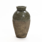 A large, textured stoneware vase with an earthy brown base and a glossy dark green upper portion on a white background exudes rustic charm.