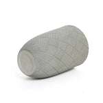 Gray cylindrical object with a textured, diamond-patterned surface, reminiscent of modern minimalist design, lies on its side against a white background.