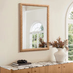An elegant decorative wall mirror with a twisted frame hangs above a wooden console table. The table, adorned with an opulent marble top, showcases a stack of books and a vase with dried flowers, creating an impeccable touch of elegant home decor.