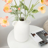 A vintage ceramic vase with pink and orange flowers graces a round table, adding rustic charm beside an open magazine.