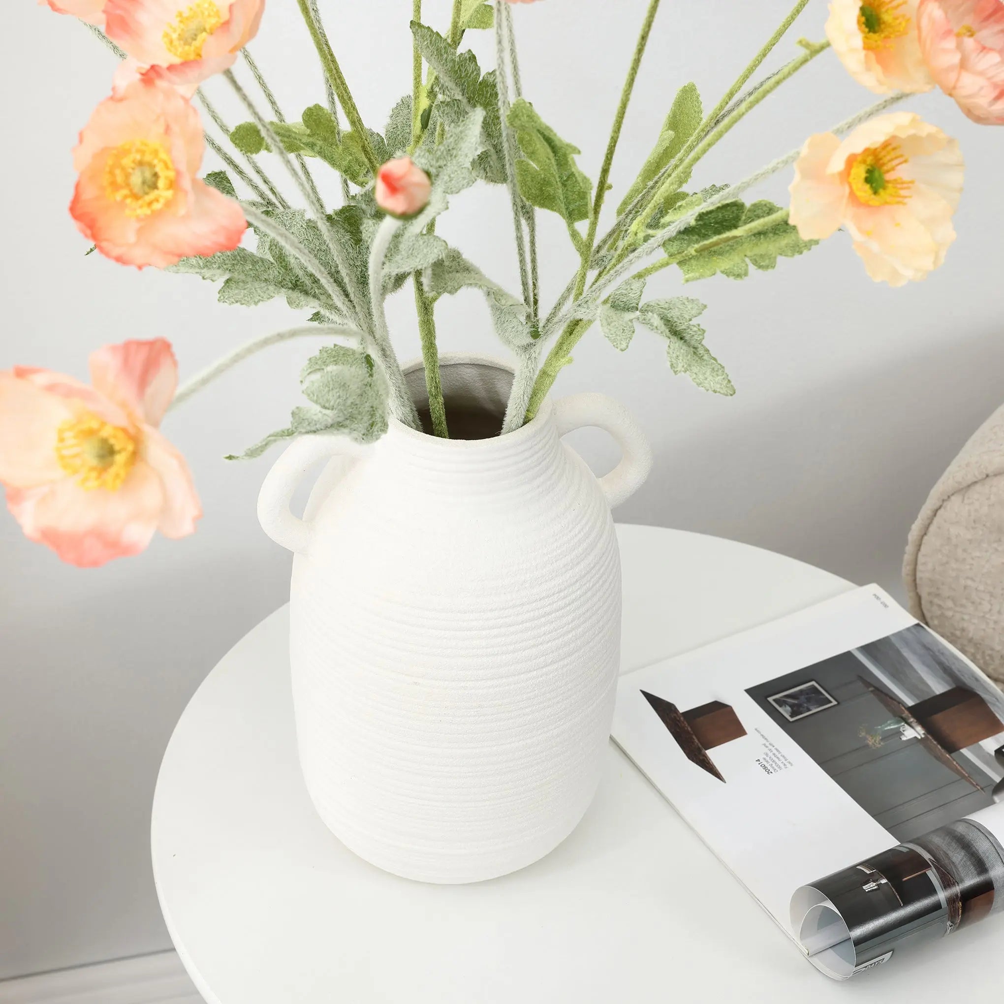 A vintage ceramic vase with pink and orange flowers graces a round table, adding rustic charm beside an open magazine.