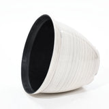 A large, cone-shaped basket with a textured surface, crafted with durable plastic construction, rests on its side against a plain background. This contemporary planter in white and black seamlessly combines modern style with functionality.