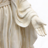 Close-up of a Mary statues outstretched hand and arm in flowing robes, crafted with a vintage ivory finish and durable magnesium oxide, set against a plain background.