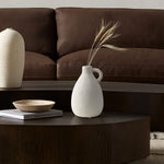 A minimalist living room scene featuring a brown leather sofa, a vintage vase with dried stems beside terracotta accents, a wooden coffee table, and stacked books perfectly captures the essence of thoughtful home decor.