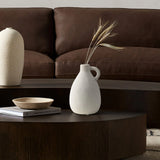A minimalist living room scene featuring a brown leather sofa, a vintage vase with dried stems beside terracotta accents, a wooden coffee table, and stacked books perfectly captures the essence of thoughtful home decor.