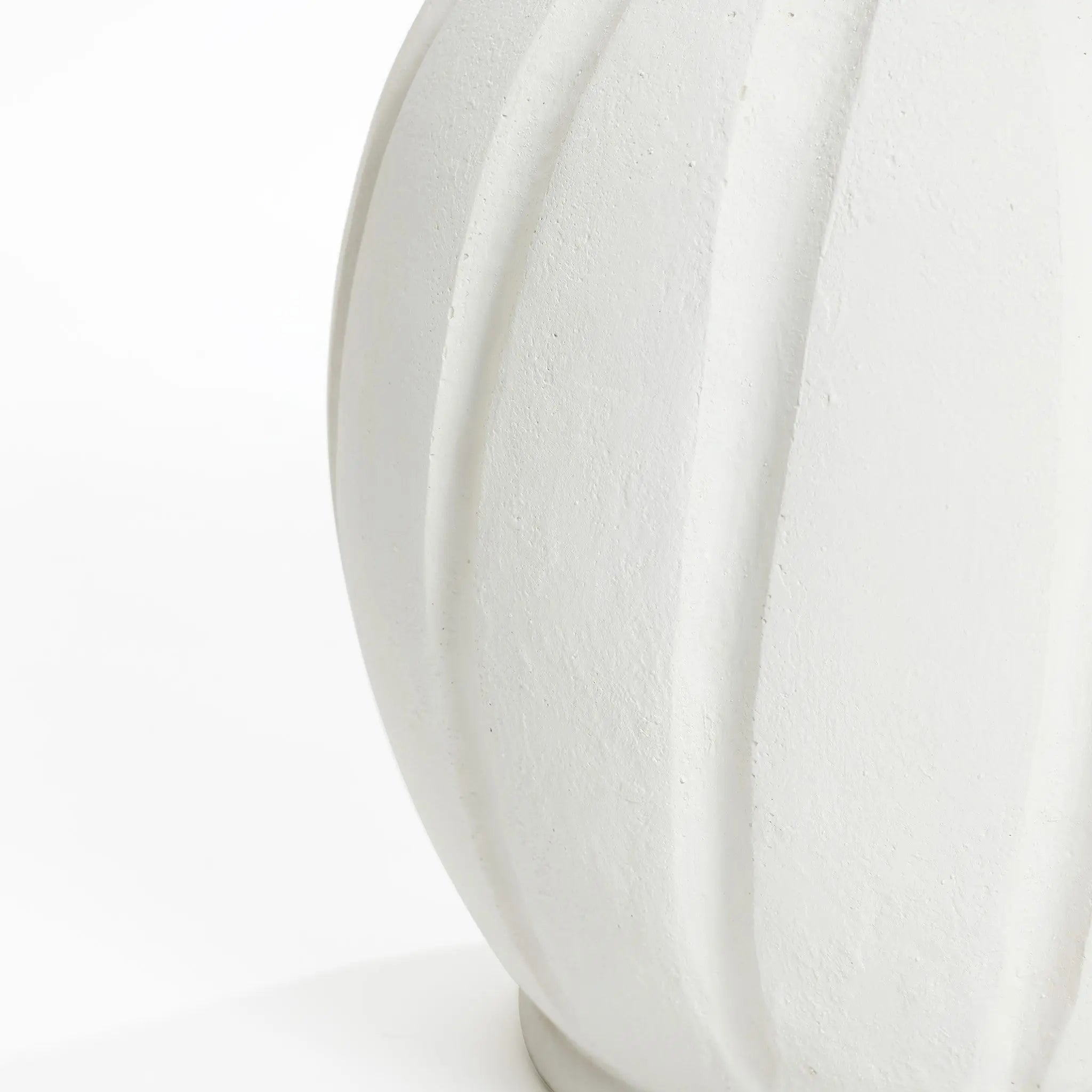 Close-up of a white textured ceramic vase with a minimalist design, featuring vertical ribbed patterns and showcasing a smooth, curved surface.