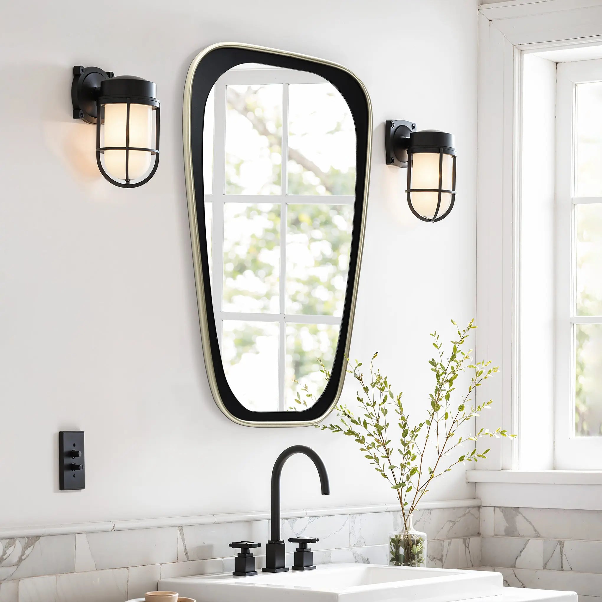 Modern bathroom with an elongated mirror, black fixtures, and two wall lights. A plant sits on the marble counter by the sink, while a window reflects the greenery outside, adding a contemporary touch to this serene space.