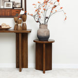 A wooden table with decorative wooden figurines and a ceramic vase filled with orange flowers sits prominently. Nearby, a mid-century modern side table features a similar vase with branches. Framed pictures adorn the wall shelf, completing the charming scene.