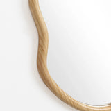 Close-up of a mirror with an irregular oval shape, set in a decorative statement frame crafted from natural pine wood, against a white background.
