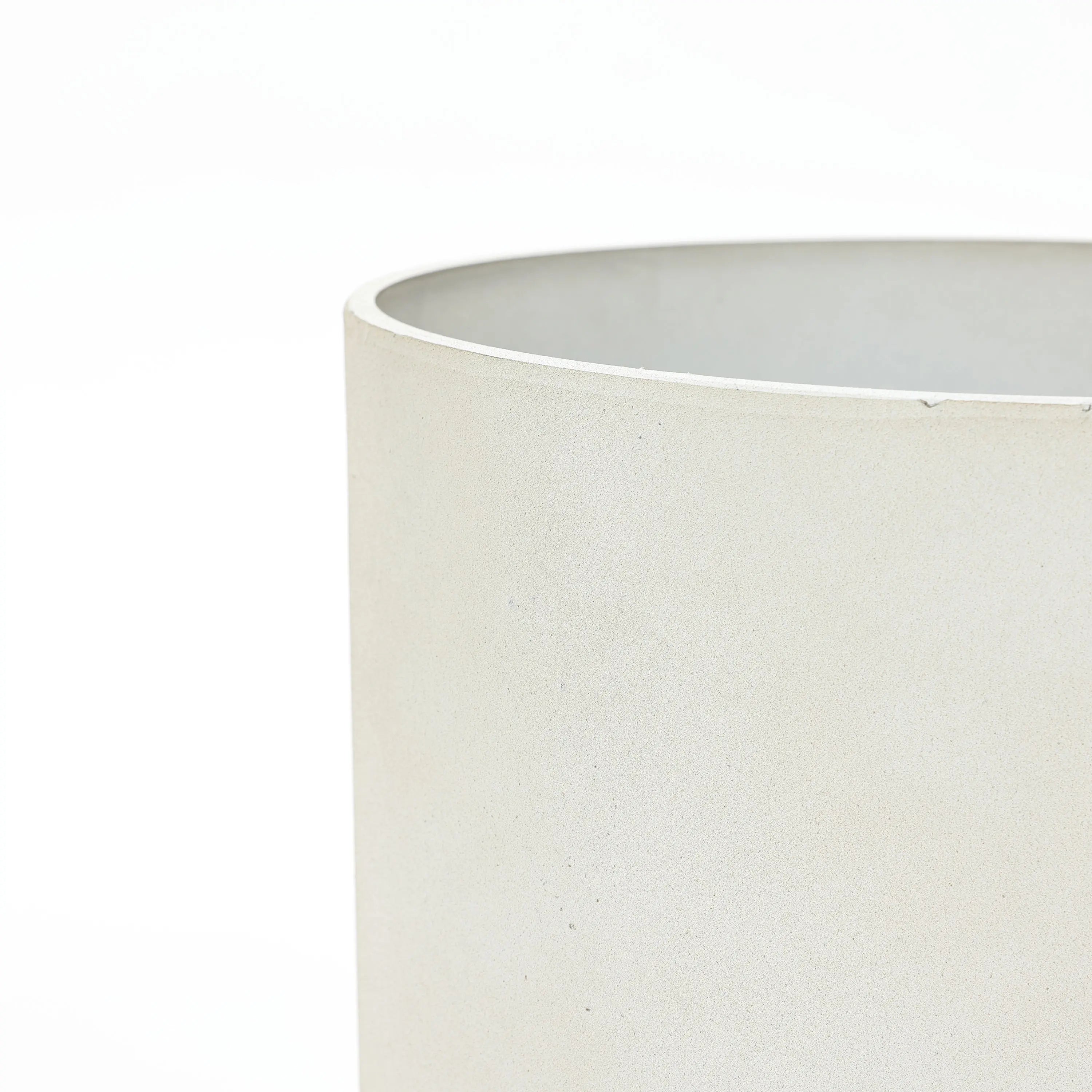 Close-up of a light beige, cylindrical ceramic planter against a white background, showcasing the smooth texture and precise edge. This contemporary piece highlights its durable design, perfect for adding elegance to any space.